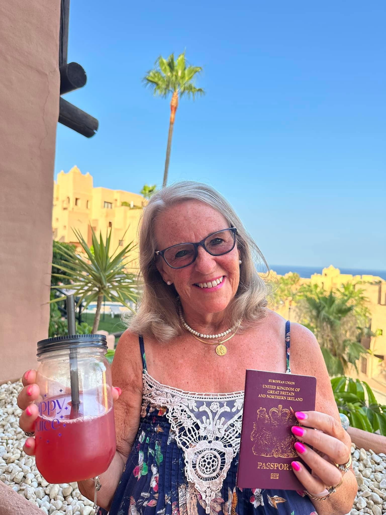 Susan Beesley holding Happy Juice and a passport with sunny background